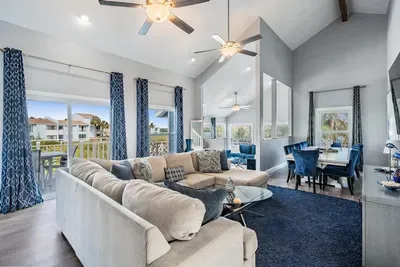Bright & inviting living space with soaring ceilings, chic décor, and floor-to-ceiling windows framing stunning water views. Relax on the plush sectional or gather at the dining table—perfect for entertaining in style!