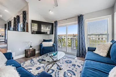 Bright & inviting second living room with bold blue seating, modern décor, and a flat-screen TV. Sliding glass doors open to a private balcony, offering fresh air, natural light, and scenic views for the perfect retreat.