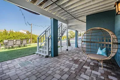 Charming covered patio with cozy egg chair, string lights, and spacious seating—perfect for lounging in shade or enjoying evening cocktails. Overlooks the yard, creating a relaxing spot for family and friends to gather.