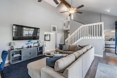 Spacious living room designed for comfort & connection! Featuring vaulted ceilings, modern décor, plush sectional seating, and a large flat-screen TV—perfect for movie nights, family gatherings, or simply relaxing in style.