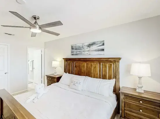 Serene bedroom retreat featuring a plush king bed with crisp white linens, rustic wood furniture, and soft ambient lighting. Relax under the ceiling fan and unwind in this bright, tranquil space designed for restful nights.