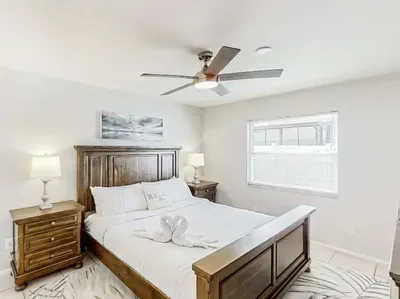 Serene bedroom retreat featuring a plush king bed, warm wood furnishings, and soft natural light. Relax beneath the ceiling fan and unwind in this peaceful, cozy space designed for total comfort.