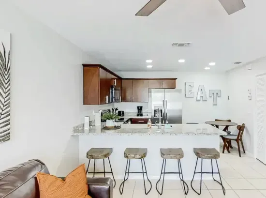 Bright, open kitchen with granite countertops, stainless-steel appliances, and warm wood cabinetry. Perfect for cooking or gathering at the chic breakfast bar with industrial stools. A cozy, inviting space that blends modern style with comfort.
