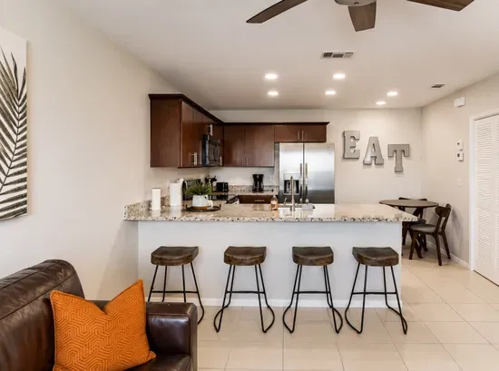 Bright, open kitchen with granite countertops, stainless-steel appliances, and warm wood cabinetry. Perfect for cooking or gathering at the chic breakfast bar with industrial stools. A cozy, inviting space that blends modern style with comfort.