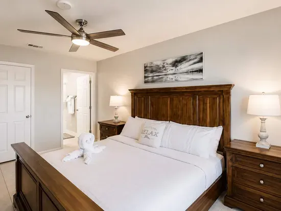 Serene bedroom retreat featuring a plush king bed with crisp white linens, rustic wood furniture, and soft ambient lighting. Relax under the ceiling fan and unwind in this bright, tranquil space designed for restful nights.