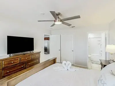 Spacious bedroom with a cozy king bed, elegant wood furniture, and a large TV for relaxing evenings. Bright and inviting with direct access to the bathroom—perfect for unwinding after a day of fun.