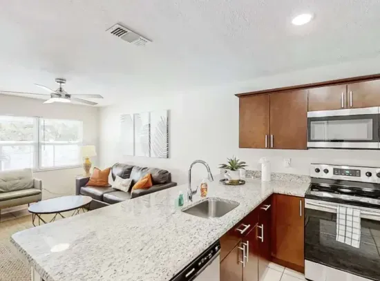 Modern kitchen with sleek granite counters, stainless-steel appliances, and rich wood cabinetry overlooking a bright, cozy living space. Perfect for cooking, entertaining, or relaxing in comfort and style.