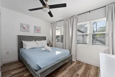 Bright and relaxing queen bedroom with warm wood floors, soft natural light, and a ceiling fan for added comfort. Enjoy fresh linens, modern décor, and a peaceful vibe—perfect for a restful night’s sleep after pool time and sunny Florida days.