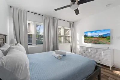 Spacious queen bedroom with a bright, airy feel and modern comfort. Enjoy a cozy bed with fresh linens, ceiling fan, wall-mounted TV, and plenty of natural light. A peaceful retreat that’s perfect for relaxing and recharging during your stay.