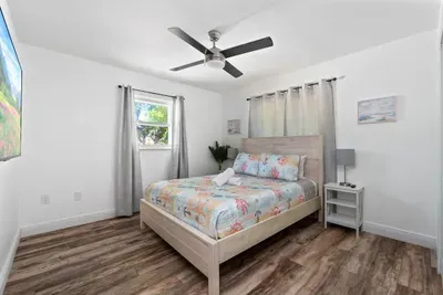 Charming and bright queen bedroom with coastal-style décor, warm wood floors, and a ceiling fan for added comfort. Enjoy fresh linens, soft lighting, and a peaceful layout—perfect for unwinding and recharging after a fun day in the sun.