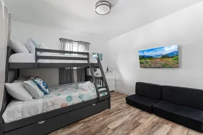 This spacious bedroom features a bunk bed plus an additional bed, a comfy futon for lounging, and a wall-mounted TV for movie nights. Bright, clean, and fun—perfect for groups needing extra sleeping and play space.