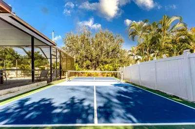 Private backyard pickleball court under sunny Florida skies! Enjoy a crisp blue playing surface, plenty of space to rally, and tropical landscaping for a resort-style feel.