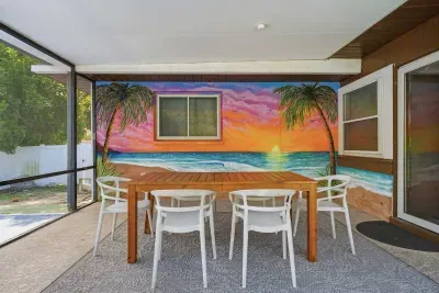 Dine under the covered lanai with a vibrant tropical sunset mural as your backdrop! Gather around the spacious table, sip morning coffee, and enjoy breezy indoor-outdoor living—steps from the screened pool and perfect for unforgettable evenings.