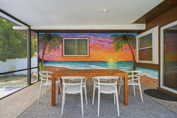 Dine under the covered lanai with a vibrant tropical sunset mural as your backdrop! Gather around the spacious table, sip morning coffee, and enjoy breezy indoor-outdoor living—steps from the screened pool and perfect for unforgettable evenings.