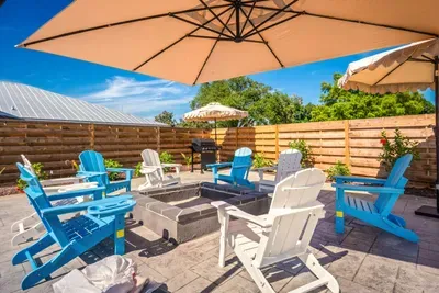 Unwind in this inviting outdoor fire pit lounge featuring cozy Adirondack seating, shaded patio umbrellas, and tropical backyard vibes.