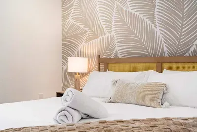 Sink into comfort in this beautifully designed bedroom featuring a plush king bed, soft neutral tones, and elegant tropical-inspired wallpaper. Cozy lighting and thoughtful details create the perfect relaxing retreat for restful vacation nights.