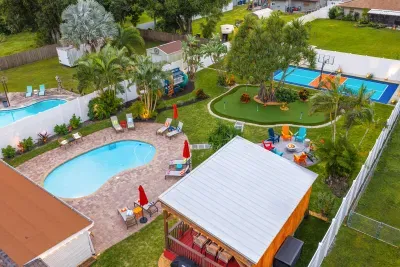 🏡 The Full Backyard, Aerial View — Heated pool, pickleball + basketball court, mini golf, gazebo, playhouse with slide, fire pit with Adirondack chairs — the whole family compound in one shot. Everything you booked for, all at once.