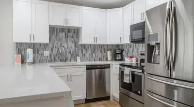 Contemporary kitchen with stainless steel appliances, sleek white cabinetry, and a stylish tile backsplash. Spacious countertops make it perfect for cooking, entertaining, or enjoying a relaxing meal at home.