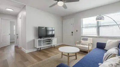 Bright and airy living room featuring a cozy blue sofa, modern armchair, and smart TV. With natural light pouring in and warm wood floors, it’s the perfect space to relax after a day of coastal adventures.