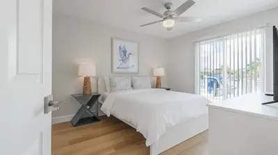 Bright and tranquil bedroom with a plush white bed, modern decor. Enjoy natural light, soft tones, and peaceful comfort for a perfect night’s rest.