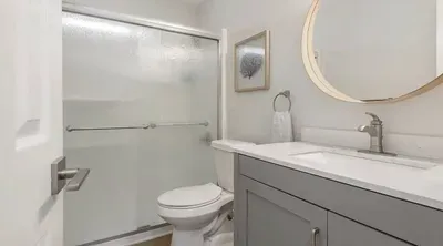 Modern bathroom with sleek gray vanity, round mirror, and glass-enclosed shower. Bright and refreshing with clean lines and soft neutral tones—perfect for a relaxing start or end to your day.
