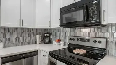 Stylish kitchen with stainless steel appliances, sleek white cabinetry, and a chic gray tile backsplash. Fully equipped for your stay—perfect for morning coffee or cooking your favorite meals in comfort.
