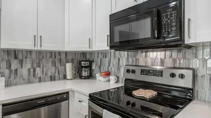 Stylish kitchen with stainless steel appliances, sleek white cabinetry, and a chic gray tile backsplash. Fully equipped for your stay—perfect for morning coffee or cooking your favorite meals in comfort.