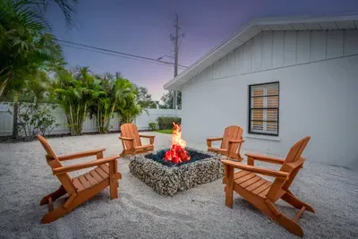 Captured at dusk, this image highlights the fire pit in full glow, casting warm light around the seating area. The chairs are perfectly positioned for gathering, while the soft twilight sky