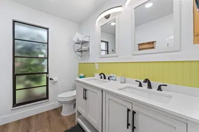 This image features a modern bathroom with a sleek double vanity in light gray, complete with elegant black faucets. The bright yellow accent wall adds a cheerful pop of color
