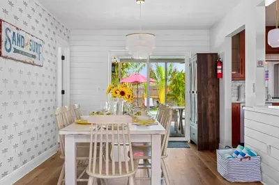 This image features a cheerful dining area with a large wooden table set for a meal. Sunflowers in a vase add a vibrant touch, while yellow plates and glasses invite guests to dine.