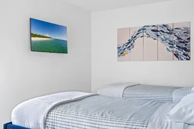 Focuses on one corner of the bedroom, highlighting the two twin beds and stylish bedding. A vibrant piece of artwork above the beds complements the tranquil color scheme.