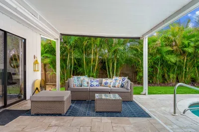 Stylish outdoor seating area with plush cushions on a rattan sofa, perfect for lounging. The space is well-defined with a patterned rug and offers a clear view of the green backyard.