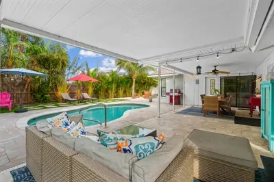 This image captures a beautifully arranged outdoor living space, complete with comfortable seating and colorful accent pillows. A glimpse of the sparkling pool and lush greenery creates a perfect backdrop.