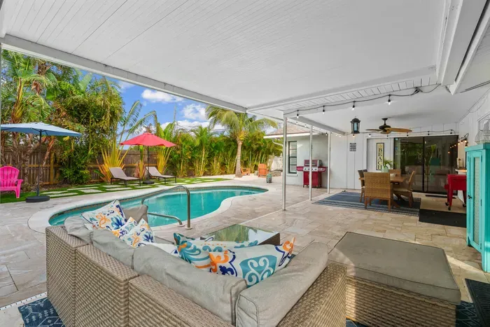 This image captures a beautifully arranged outdoor living space, complete with comfortable seating and colorful accent pillows. A glimpse of the sparkling pool and lush greenery creates a perfect backdrop.