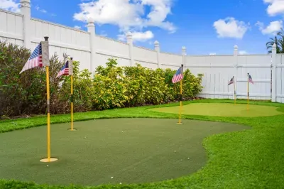 This image showcases a well-manicured putting green set against a white fence, with lush green grass surrounding the area. Several small American flags are placed near each hole, adding a playful touch.