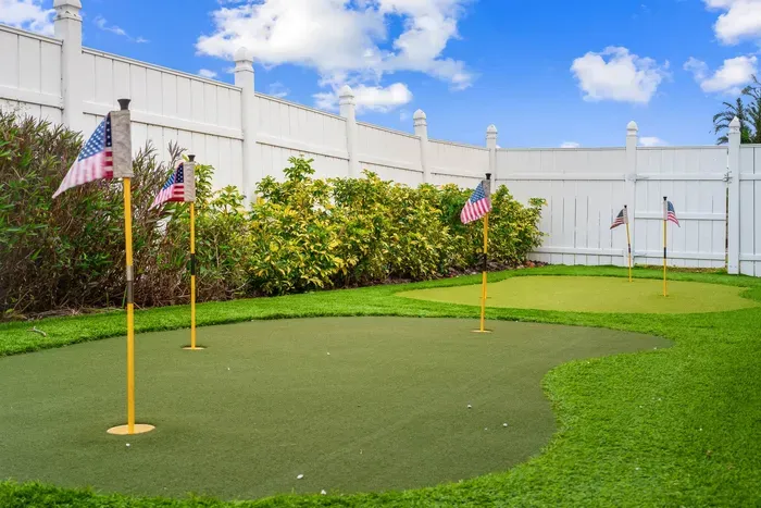 This image showcases a well-manicured putting green set against a white fence, with lush green grass surrounding the area. Several small American flags are placed near each hole, adding a playful touch.