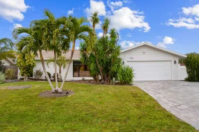 This photo captures the welcoming facade of the Airbnb property, featuring a single-story house surrounded by tropical plants and palm trees. The neatly paved driveway leads to a spacious garage.