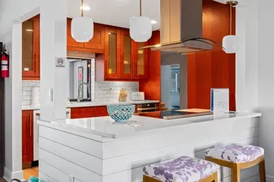 This image features a modern kitchen bar with a white quartz countertop and sleek wooden cabinets. Three stylish pendant lights hang above, illuminating a decorative blue bowl.