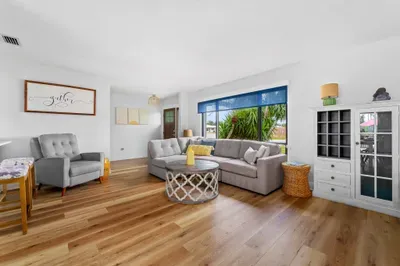 This shot presents an inviting living area with a comfortable gray sectional and a lovely blue window treatment. A round coffee table with intricate detailing sits in the center, surrounded by light wood accents and additional seating options.