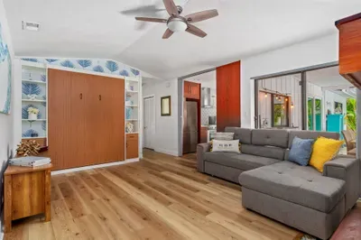 This photo showcases a spacious lounge area with a comfortable gray sectional sofa and a ceiling fan overhead. A stylish built-in bookshelf holds decorative items and provides storage space.