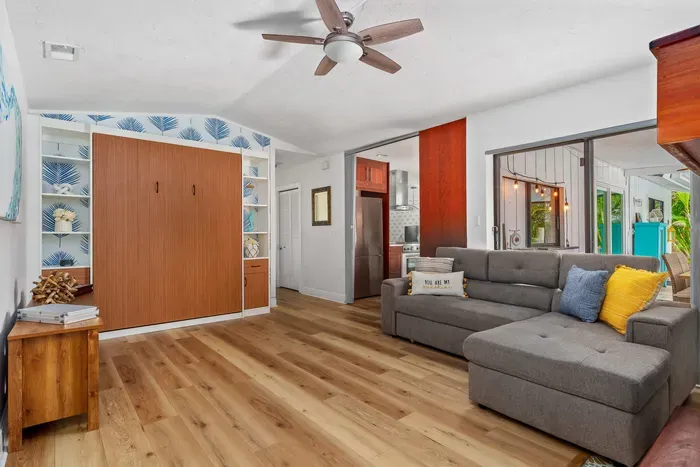 This photo showcases a spacious lounge area with a comfortable gray sectional sofa and a ceiling fan overhead. A stylish built-in bookshelf holds decorative items and provides storage space.