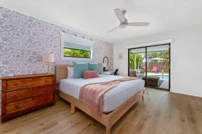 This photo shows a spacious bedroom filled with natural light. The floral wallpaper, soft bedding, and wooden dresser create a harmonious and cozy space. Large glass doors lead to an outdoor area, inviting guests to enjoy the fresh air.