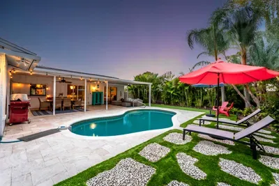 Captured at dusk, this photo reveals the enchanting ambiance of the pool area with warm lighting illuminating the space. The red umbrella and cozy seating area invite relaxation as the sun sets, creating a perfect evening retreat.