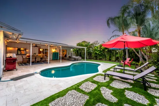 Captured at dusk, this photo reveals the enchanting ambiance of the pool area with warm lighting illuminating the space. The red umbrella and cozy seating area invite relaxation as the sun sets, creating a perfect evening retreat.