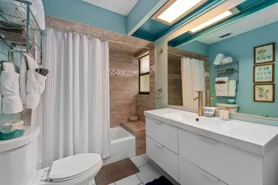 Stylish bathroom featuring a sleek white vanity with modern fixtures. A large mirror reflects the soft blue walls adorned with decorative art. A glass-enclosed shower with textured tiles is visible, along with neatly arranged towels on a nearby rack.