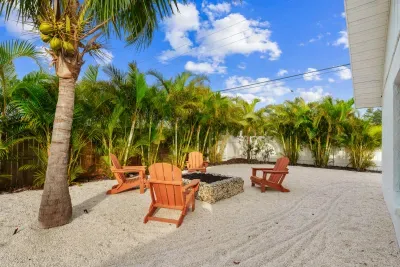 From a slightly different angle, this photo focuses on the same fire pit area, surrounded by vibrant greenery. The sunlit space is dotted with palm trees and showcases the natural beauty of the surroundings, making it an ideal spot for relaxation