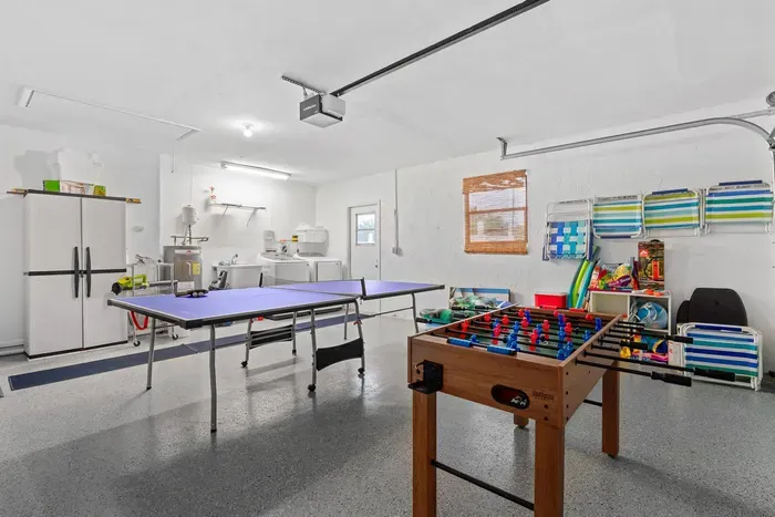 Spacious multi-purpose room featuring a ping pong table and a foosball table, perfect for indoor entertainment. The floor has a smooth finish, and a large refrigerator is visible in the background alongside other storage item