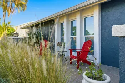 Inviting front patio with vibrant red Adirondack chairs and lush greenery. A peaceful spot to enjoy your morning coffee or unwind in the evening breeze.