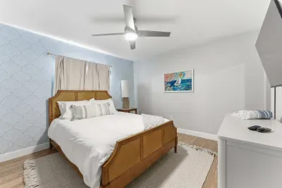 Bright and cozy bedroom featuring a warm wood bed frame, soft blue accent wall, and beach-inspired artwork. A perfect mix of comfort and charm for a peaceful night’s rest.
