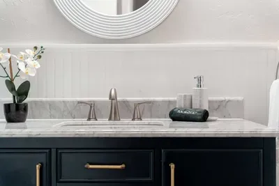 Elegant vanity with marble countertop, brushed nickel fixtures, and a navy cabinet accented by gold hardware. A fresh orchid and modern details add a touch of luxury to this serene bathroom space.